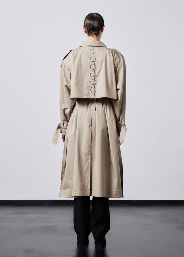 INTERNATIONAL CITIZEN.  Style: The Equinox Trench Coat, is voluminous, it features classic trench coat detailing and optional 7-Chakra ring detail at the back storm flap. Unisex item. Full back view.  Made of Italian Organic Cotton, Dune. Spiritually Infused, Sustainable Luxury Fashion in Berlin.