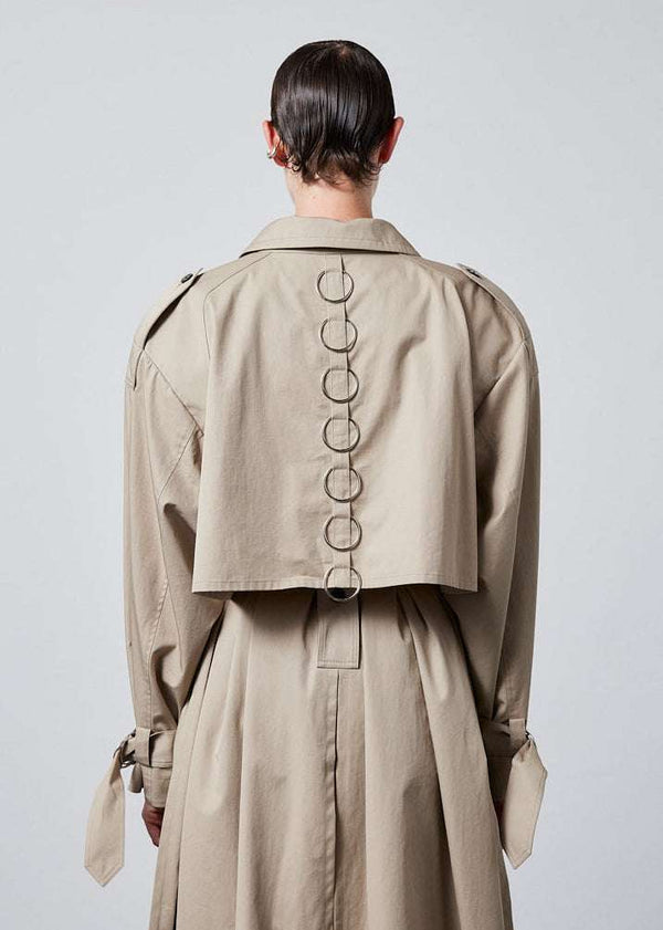 INTERNATIONAL CITIZEN.  Style: The Equinox Trench Coat, is voluminous and it features classic trench coat detailing, removable shoulder pads and optional 7-Chakra ring detail at the back storm flap. Unisex item. Close up back view.  Made of Italian Organic Cotton, Dune. Spiritually Infused, Sustainable Luxury Fashion in Berlin.