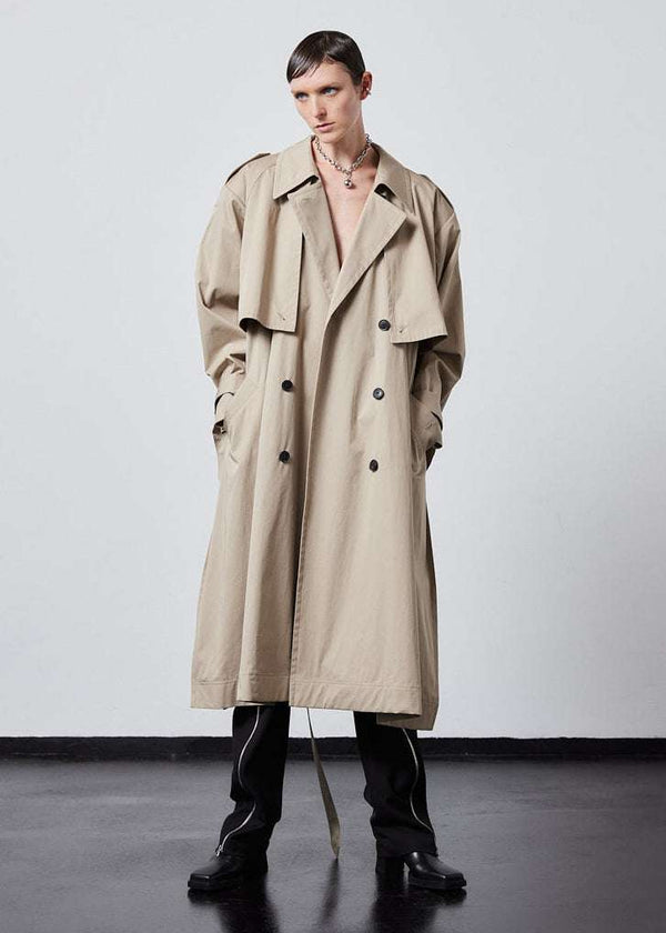 INTERNATIONAL CITIZEN.  Style: The Equinox Trench Coat, is voluminous and features classic trench coat detailing, overlapping sides seams at the underarm, removable shoulder pads. Unisex item.  Full front view un-belted. Made of Italian Organic Cotton, Dune. Spiritually Infused, Sustainable Luxury Fashion in Berlin.