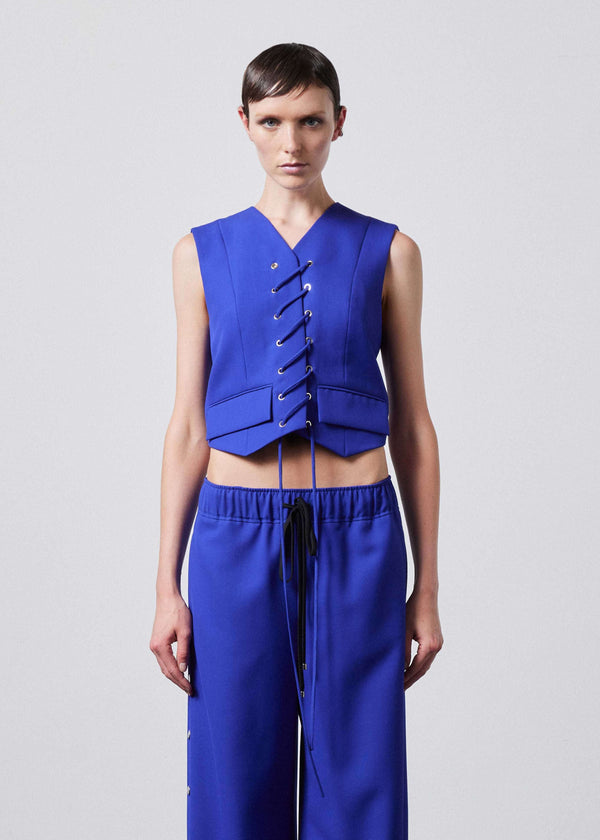 INTERNATIONAL CITIZEN.  Style: The Stitch Vest features a high neckline with overlapping front closure held with an eyelet stitch lacing detail. Made of Italian Wool RWS, Lapis Lazuli Blue. Spiritually Infused, Sustainable Luxury Fashion in Berlin. Front photo.