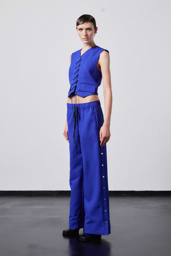 INTERNATIONAL CITIZEN.  Style: The Stitch Vest features a high neckline with overlapping front closure held with an eyelet stitch lacing detail. Made of Italian Wool RWS, Lapis Lazuli Blue. Spiritually Infused, Sustainable Luxury Fashion in Berlin. Full side front photo.