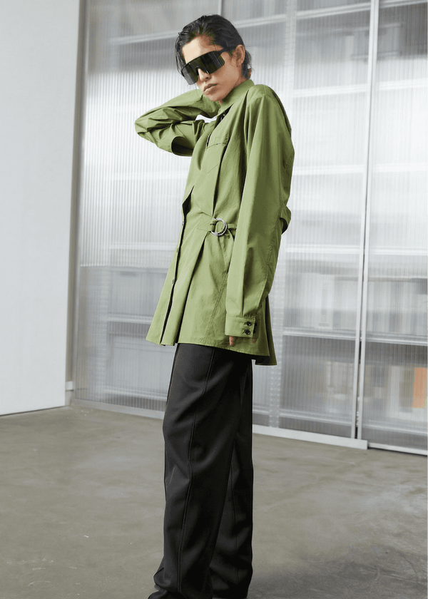 INTERNATIONAL CITIZEN.  Style: Artist Shirt Dress. Side front view. The style has an oversized shirt with a pen pocket at the chest, open underarms for breathability, and back belt ties that adjust at the front with silver rings. The shirt are made of Italian organic Cotton Twill in Nephrite Jade. Spiritually Infused, Sustainable Luxury Fashion in Berlin.