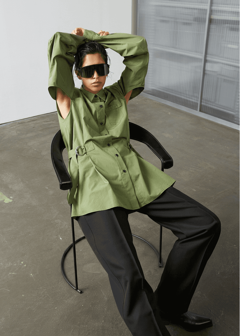 INTERNATIONAL CITIZEN.  Style: Artist Shirt Dress. Front View seated. The style has an oversized shirt with a pen pocket at the chest, open underarms for breathability, and back belt ties that adjust at the front with silver rings. The shirt are made of Italian organic Cotton Twill in Nephrite Jade. Spiritually Infused, Sustainable Luxury Fashion in Berlin.