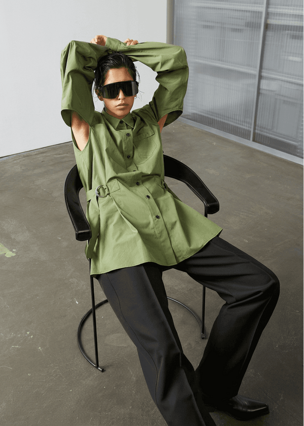 INTERNATIONAL CITIZEN.  Style: Artist Shirt Dress. Front View seated. The style has an oversized shirt with a pen pocket at the chest, open underarms for breathability, and back belt ties that adjust at the front with silver rings. The shirt are made of Italian organic Cotton Twill in Nephrite Jade. Spiritually Infused, Sustainable Luxury Fashion in Berlin.