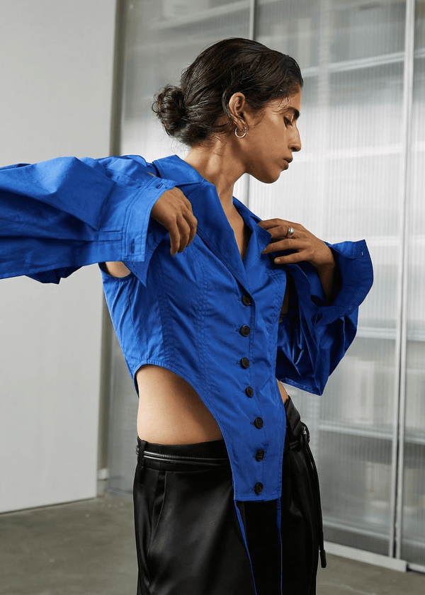 INTERNATIONAL CITIZEN.  Style: A French Cut Button Bodysuit with tie closures. It features exaggerated sleeve volume pleated at the cuffs, with an open under arm for breathability. Made of Italian Organic Cotton, Lapis lazuli Blue. Spiritually Infused, Sustainable Luxury Fashion in Berlin.