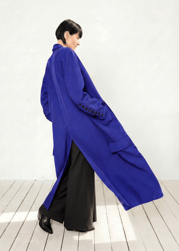 INTERNATIONAL CITIZEN.  Style: Duster Coat. A unisex coat that features traditional men's tailoring construction details. Side View. The coat is made of Italian RWS Wool in Lapis Lazuli Blue. Spiritually Infused, Sustainable Luxury Fashion in Berlin.
