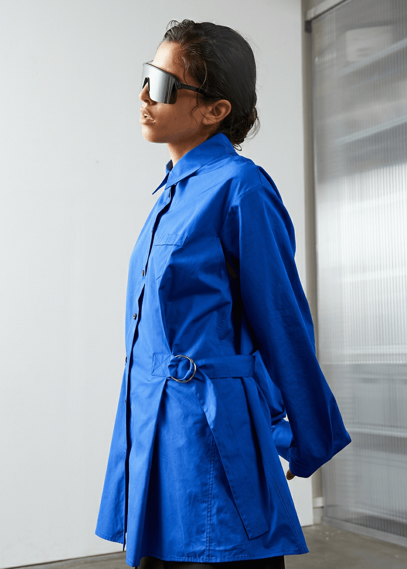 INTERNATIONAL CITIZEN.  Style: Artist Shirt. Side view. Style has an oversized shirt with a pen pocket at the chest and back belt ties that adjust at the front with silver rings. The shirt are made of Italian organic Cotton in Lapis Lazuli Blue. Spiritually Infused, Sustainable Luxury Fashion in Berlin.