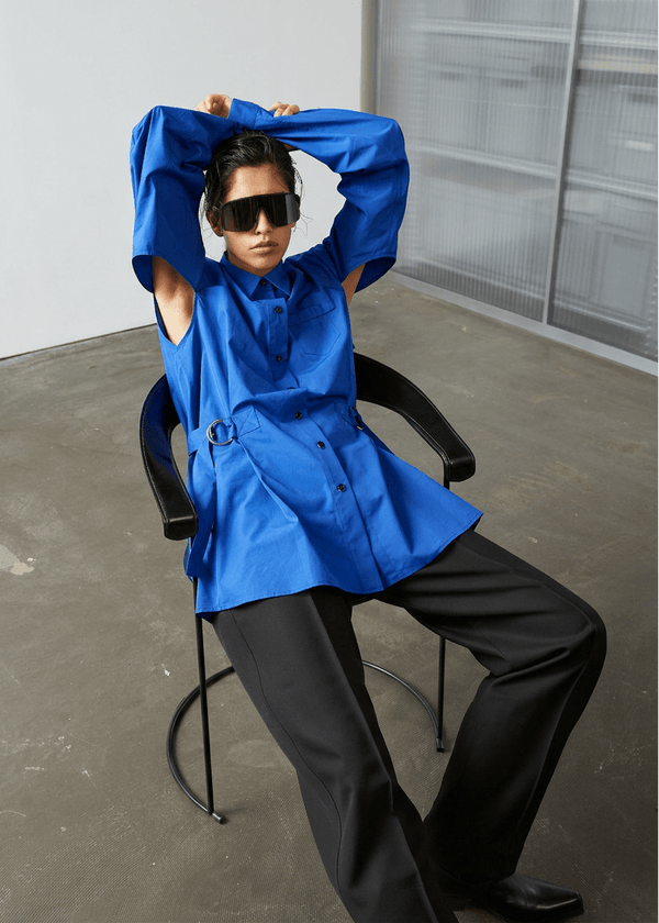 INTERNATIONAL CITIZEN.  Style: Artist Shirt. Style has an oversized shirt with a pen pocket at the chest, open underarms for breathability, and back belt ties that adjust at the front with silver rings. The shirt are made of Italian organic Cotton in Lapis Lazuli Blue. Spiritually Infused, Sustainable Luxury Fashion in Berlin.