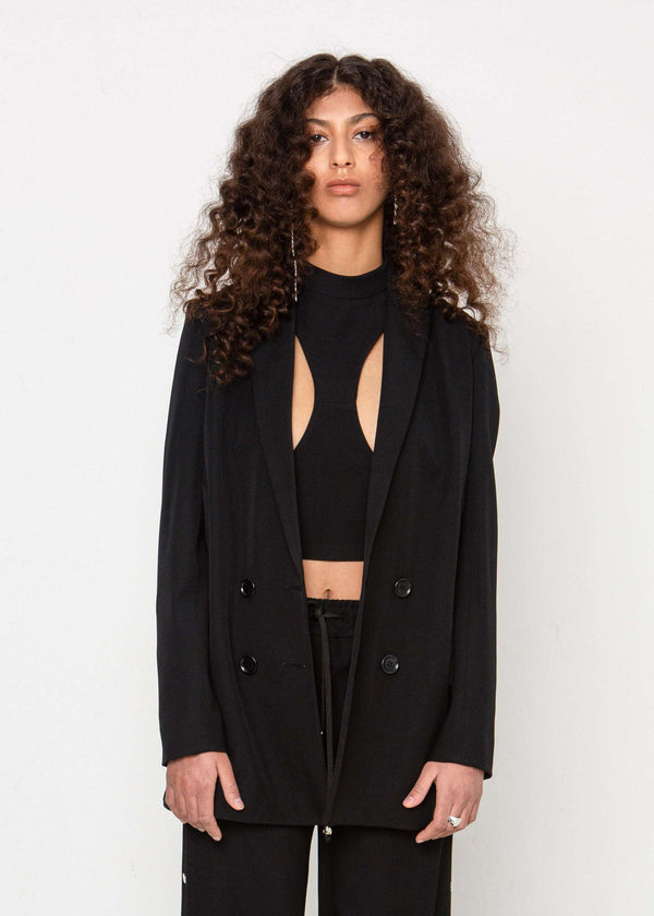 INTERNATIONAL CITIZEN.  Style: The Heart Opener Jacket features slim sleeves cut on the bias, a clean fitted shoulder and straight body, creating a cool silhouette that can be belted for an hourglass shape. Close up photo. Made of Italian Wool, certified (RWS) Responsible Wool Standard, Obsidian Black. Spiritually Infused, Sustainable Luxury Fashion in Berlin.