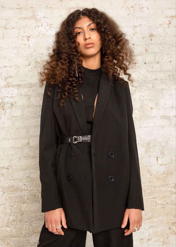 INTERNATIONAL CITIZEN.  Style: The Heart Opener Jacket features slim sleeves cut on the bias, a clean fitted shoulder and straight body, belted different ways.  Close up front photo. Close up photo. Made of Italian Wool, certified (RWS) Responsible Wool Standard, Obsidian Black. Spiritually Infused, Sustainable Luxury Fashion in Berlin.