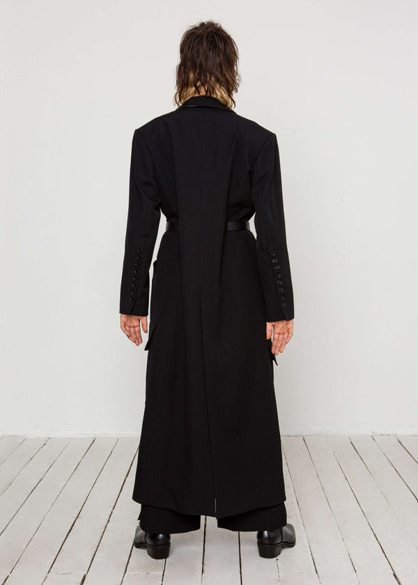 INTERNATIONAL CITIZEN.  Style: Duster Coat. A unisex coat that features traditional men's tailoring construction details. Male model back view. The coat is made of Italian RWS Wool in Obsidian Black. Spiritually Infused, Sustainable Luxury Fashion in Berlin.