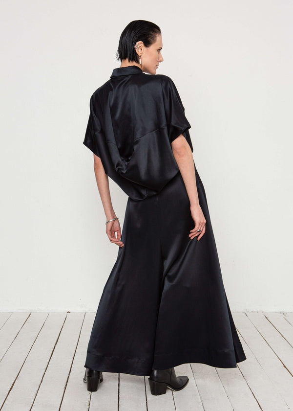 INTERNATIONAL CITIZEN.  Style: Prism Top, using sacred geometry of a 3-dimensional prism falling over the body in a soft cowl drape with an origami folded collar at the front placket. Made of Organic Silk, Obsidian Black. Spiritually Infused, Sustainable Luxury Fashion in Berlin. Full body back photo.