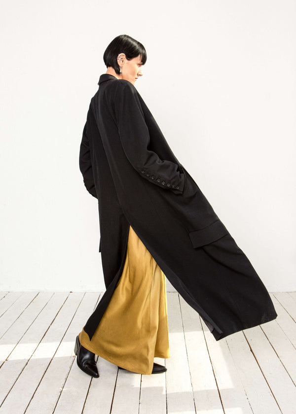 INTERNATIONAL CITIZEN.  Style: Duster Coat. A unisex coat that features traditional men's tailoring construction details. Side view. The coat is made of Italian RWS Wool in Obsidian Black. Spiritually Infused, Sustainable Luxury Fashion in Berlin.