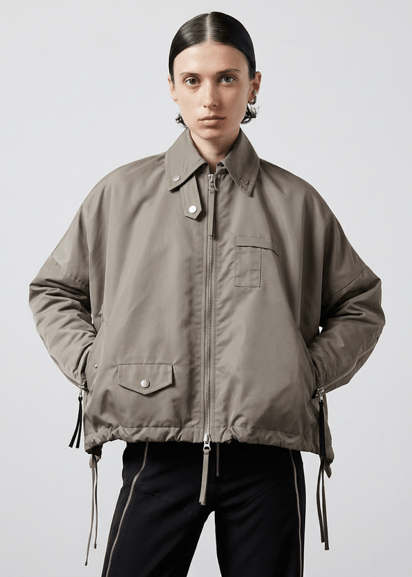 INTERNATIONAL CITIZEN.  Style: The Cube Coat, is a 3D cube tilted on its axes to create a boxy minimal front body. It has zipper closures, and a drawcord at the front hemline and a utility pen pocket on the chest. Unisex style. Made of Italian post-consumer recycled Nylon, Dune. Spiritually Infused, Sustainable Luxury Fashion in Berlin.