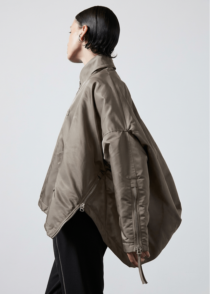 INTERNATIONAL CITIZEN.  Style: The Cube Coat, is a 3D cube tilted on its axes to create a boxy minimal front body and dramatic drape in the back body. It has zipper closures, and a drawcord at the front hemline. Side view. Unisex style. Made of Italian post-consumer recycled Nylon, Dune. Spiritually Infused, Sustainable Luxury Fashion in Berlin.