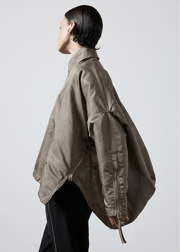 INTERNATIONAL CITIZEN.  Style: The Cube Coat, is a 3D cube tilted on its axes to create a boxy minimal front body and dramatic drape in the back body. It has zipper closures, and a drawcord at the front hemline. Side view. Unisex style. Made of Italian post-consumer recycled Nylon, Dune. Spiritually Infused, Sustainable Luxury Fashion in Berlin.