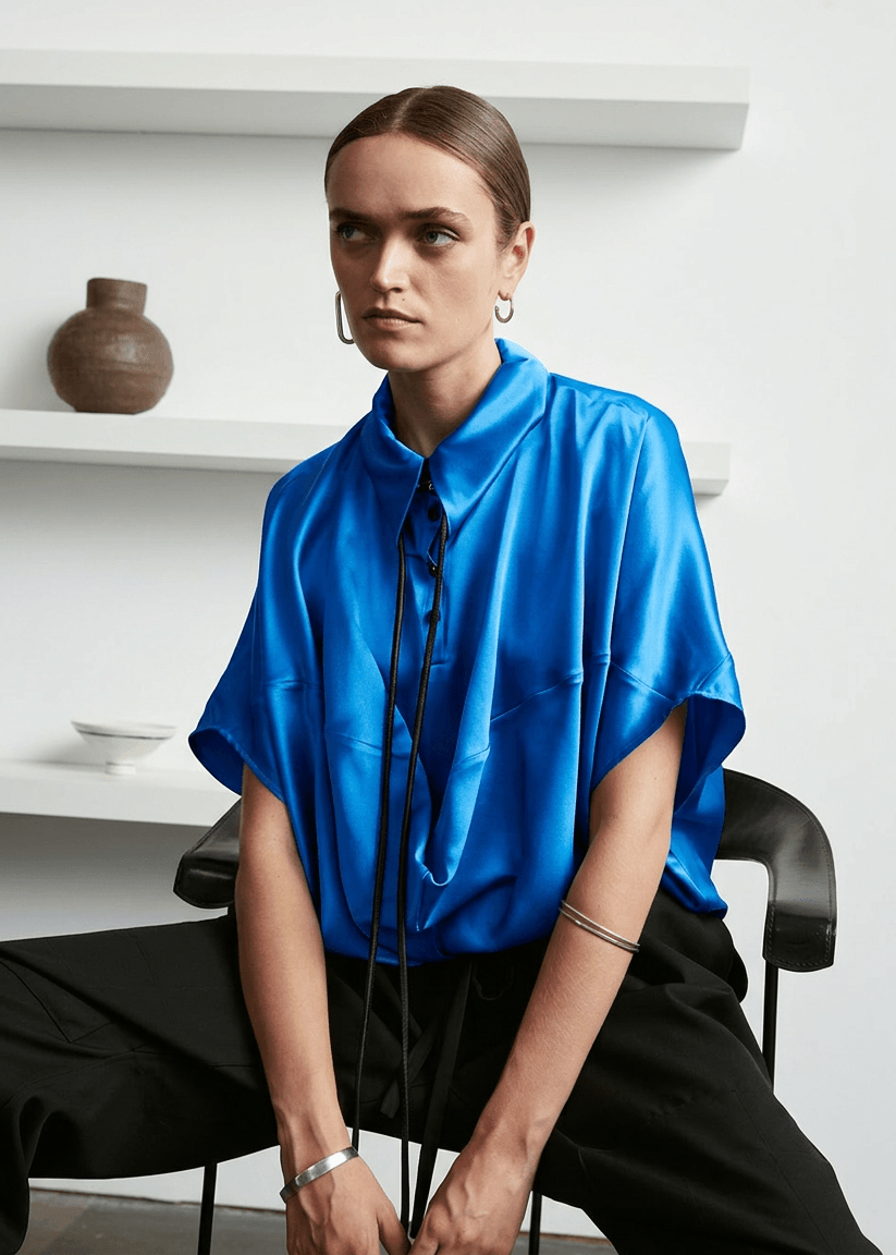 INTERNATIONAL CITIZEN.  Style: Prism Top, using sacred geometry of a 3-dimensional prism falling over the body in a soft cowl drape with an origami folded collar at the front placket. Made of Organic Silk, Azurite Blue. Spiritually Infused, Sustainable Luxury Fashion in Berlin.