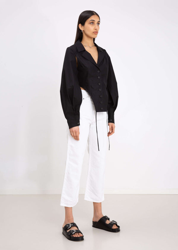 INTERNATIONAL CITIZEN.  Style: A French Cut Button Bodysuit with tie closures. It features exaggerated sleeve volume pleated at the cuffs. Side front view. Made of Italian Organic Cotton, White Quartz. Spiritually Infused, Sustainable Luxury Fashion in Berlin.