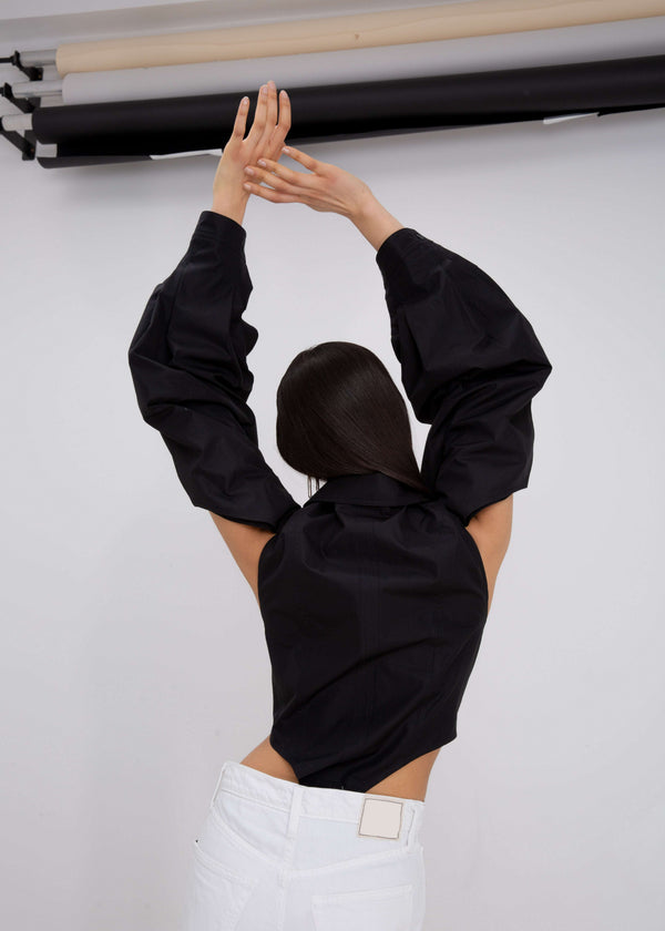 INTERNATIONAL CITIZEN.  Style: A French Cut Button Bodysuit with tie closures. It features exaggerated sleeve volume pleated at the cuffs, with an open under arm for breathability. Close up back view.  Made of Italian Organic Cotton, Obsidian Black. Spiritually Infused, Sustainable Luxury Fashion in Berlin.