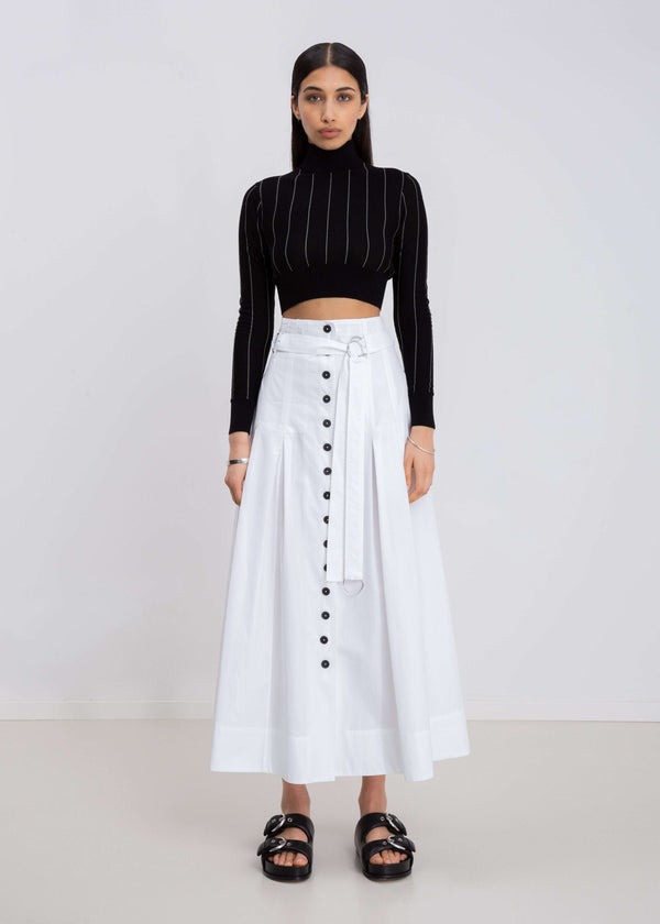 INTERNATIONAL CITIZEN.  Style: Button Skirt. Front full body view. A Button Skirt with box pleats below the hips. Detachable belt with silver ring details for closure. The skirt is made of Italian organic Cotton in White Quartz. Spiritually Infused, Sustainable Luxury Fashion in Berlin.