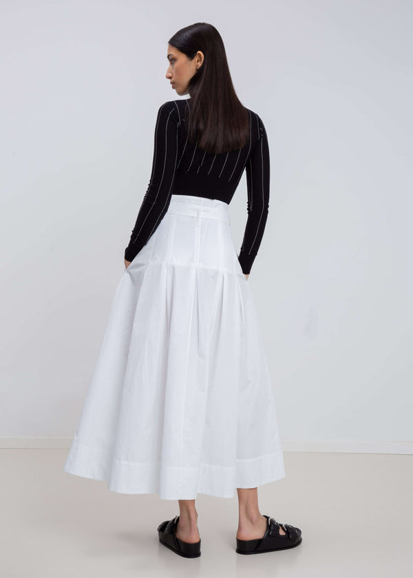 INTERNATIONAL CITIZEN.  Style: Button Skirt. Back full body view. A Button Skirt with box pleats below the hips. Detachable belt with silver ring details for closure. The skirt is made of Italian organic Cotton in White Quartz. Spiritually Infused, Sustainable Luxury Fashion in Berlin.