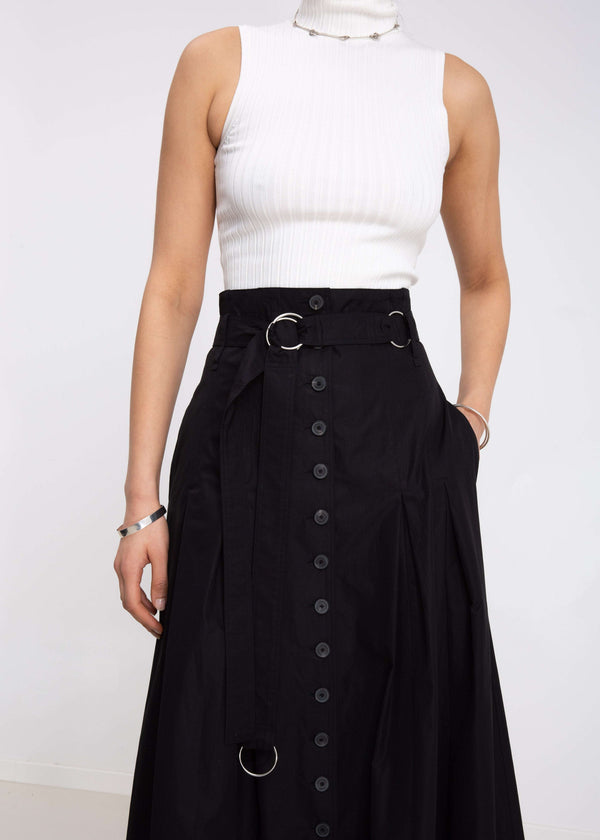 INTERNATIONAL CITIZEN.  Style: Button Skirt. Close up front view. A Button Skirt with box pleats below the hips. Detachable belt with silver ring details for closure. The skirt is made of Italian organic Cotton in Obsidian Black. Spiritually Infused, Sustainable Luxury Fashion in Berlin.