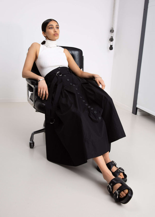 INTERNATIONAL CITIZEN.  Style: Button Skirt.  A Button Skirt with box pleats below the hips. Detachable belt with silver ring details for closure. The skirt is made of Italian organic Cotton in Obsidian Black. Spiritually Infused, Sustainable Luxury Fashion in Berlin.