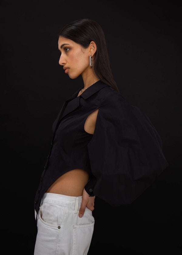 INTERNATIONAL CITIZEN.  Style: A French Cut Button Bodysuit with tie closures. It features exaggerated sleeve volume pleated at the cuffs, with an open under arm for breathability. Side profile view. Made of Italian Organic Cotton, Obsidian Black. Spiritually Infused, Sustainable Luxury Fashion in Berlin.