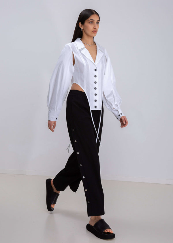 INTERNATIONAL CITIZEN.  Style: A French Cut Button Bodysuit with tie closures. It features exaggerated sleeve volume pleated at the cuffs, with an open under arm for breathability. Made of Italian Organic Cotton, White Quartz. Spiritually Infused, Sustainable Luxury Fashion in Berlin.