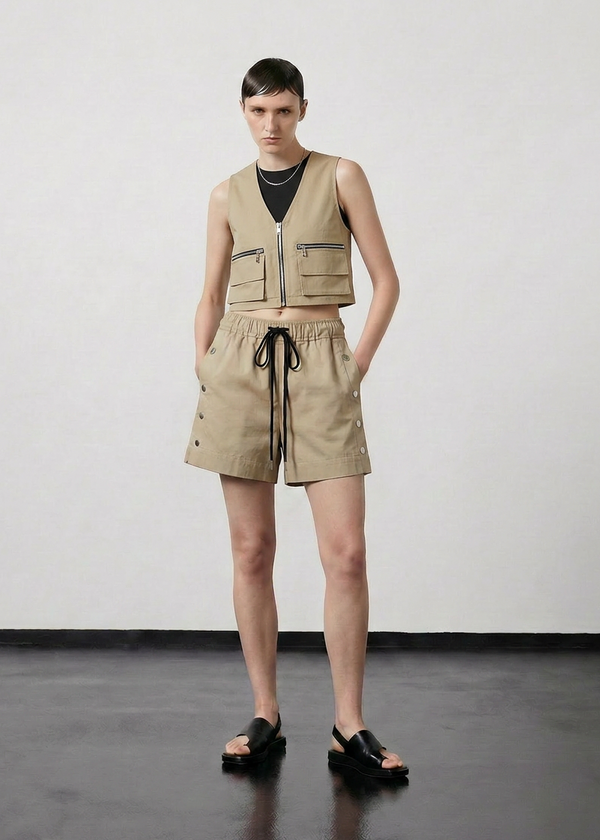 INTERNATIONAL CITIZEN.  Style: The Track Short has a smooth back waistband and elastic front with a drawcord tunnel at the front. Silver metal snaps down the side and mid thigh length. Full front view. Unisex item. Made of Italian Organic Cotton Twill, Dune. Spiritually Infused, Sustainable Luxury Fashion in Berlin.