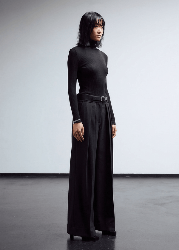 INTERNATIONAL CITIZEN.  Style: The Deep Pleated Pant, falls below the natural waist. The pleats nearly meet at the center front. Side front view. Made of Italian RWS Wool, Obsidian Black Purple. Spiritually Infused, Sustainable Luxury Fashion in Berlin.